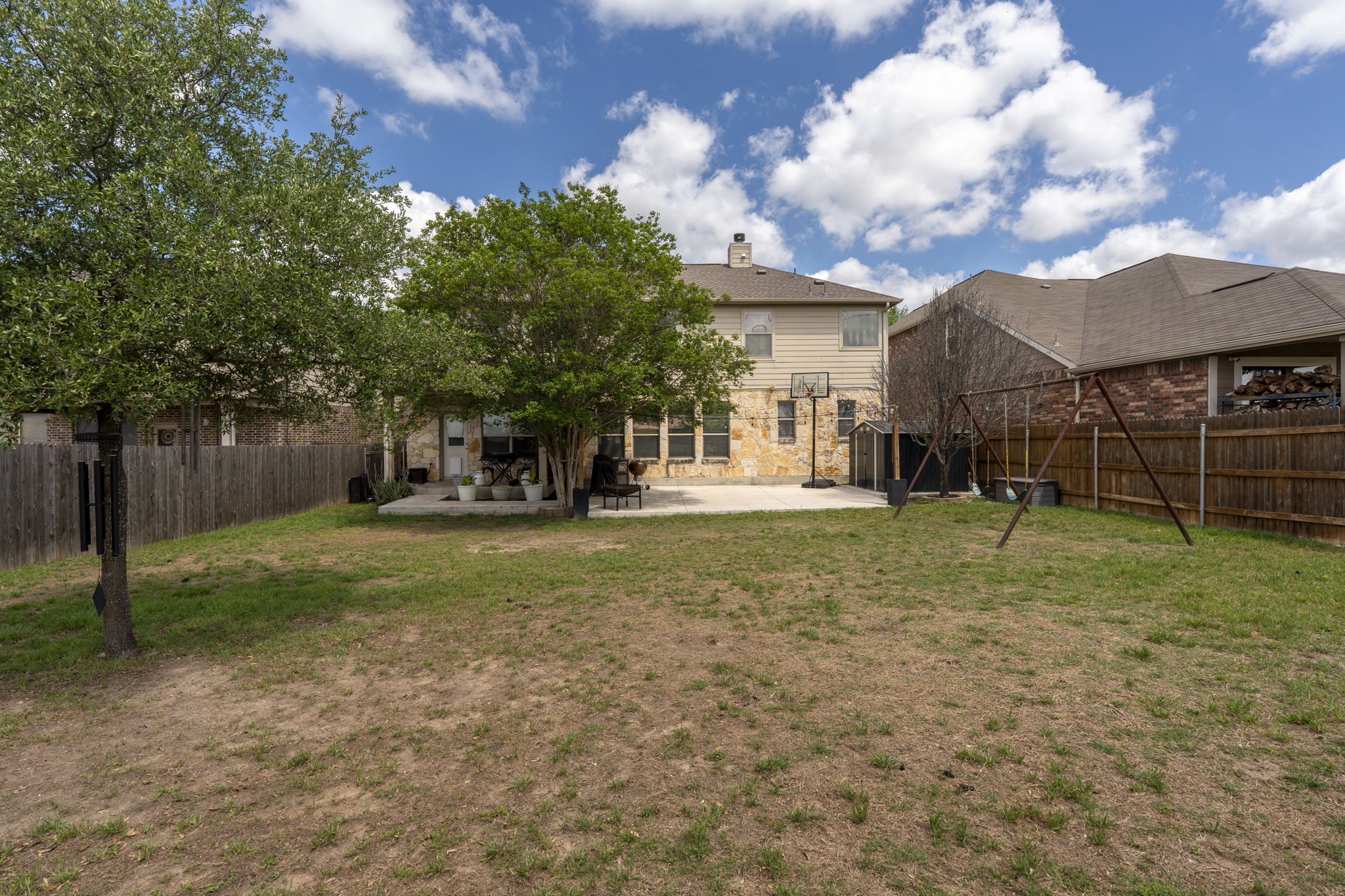 227 Sandstone Trail Buda, TX 78610 - Photo 25 of 33 Expansive backyard featuring a concrete patio, mature trees, and a full wood privacy fence