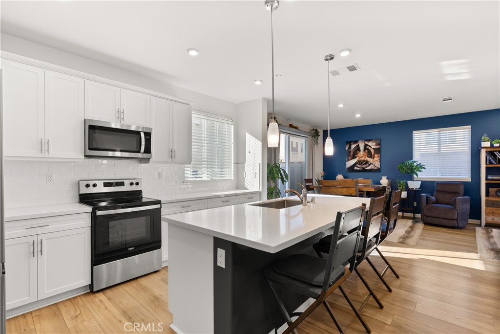 904 Maya Crossing, Unit 19 Lake Elsinore, CA 92530 - Photo 8 of 25 a kitchen with stainless steel appliances granite countertop a stove a refrigerator a kitchen island a sink a stove and white cabinets with wooden floor
