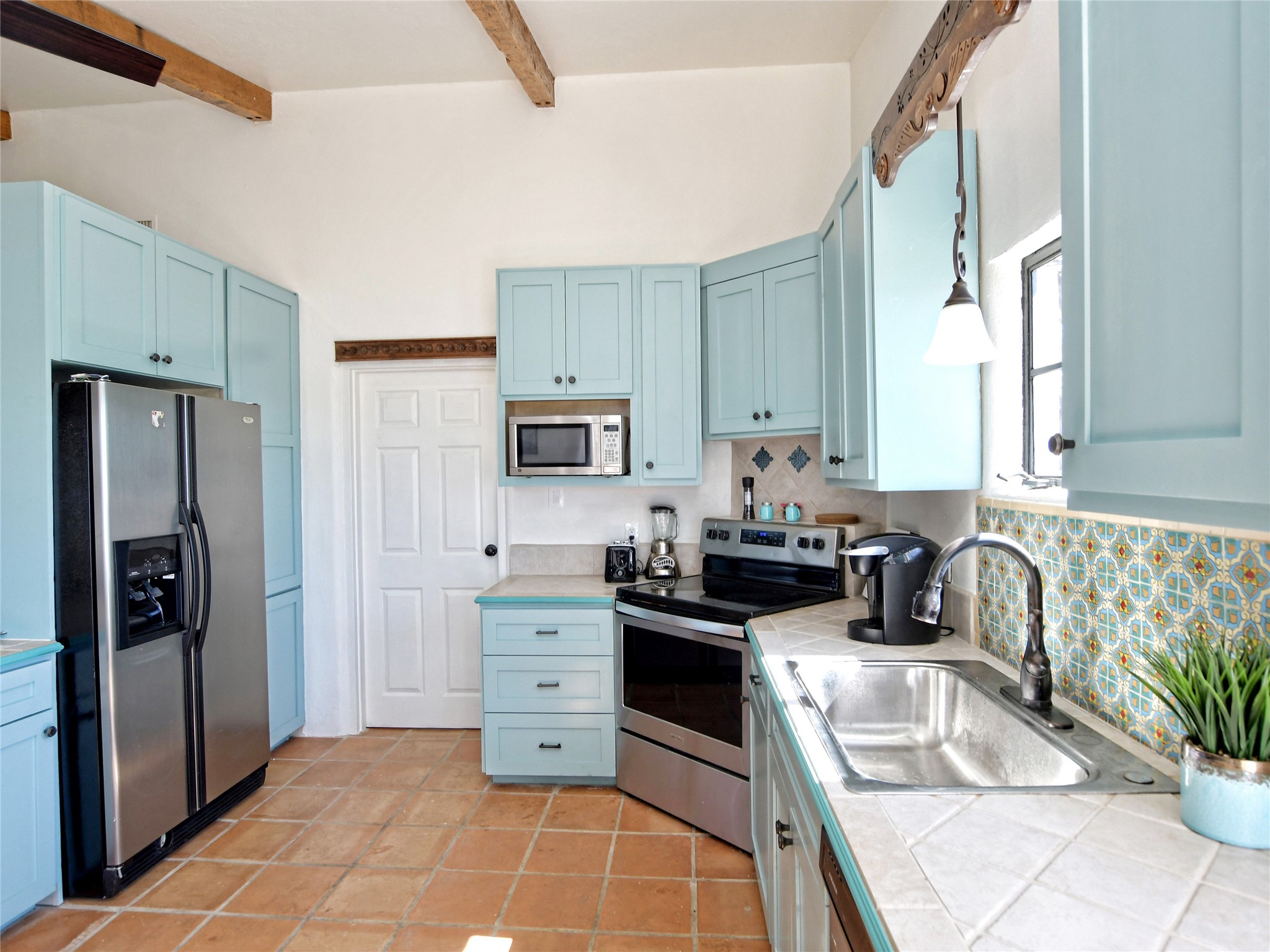 17123 Rocky Ridge Road Austin, TX 78734 - Photo 14 of 26 Kitchen featuring light blue cabinetry, stainless steel appliances, terracotta tile flooring, patterned backsplash, and exposed wood ceiling beams