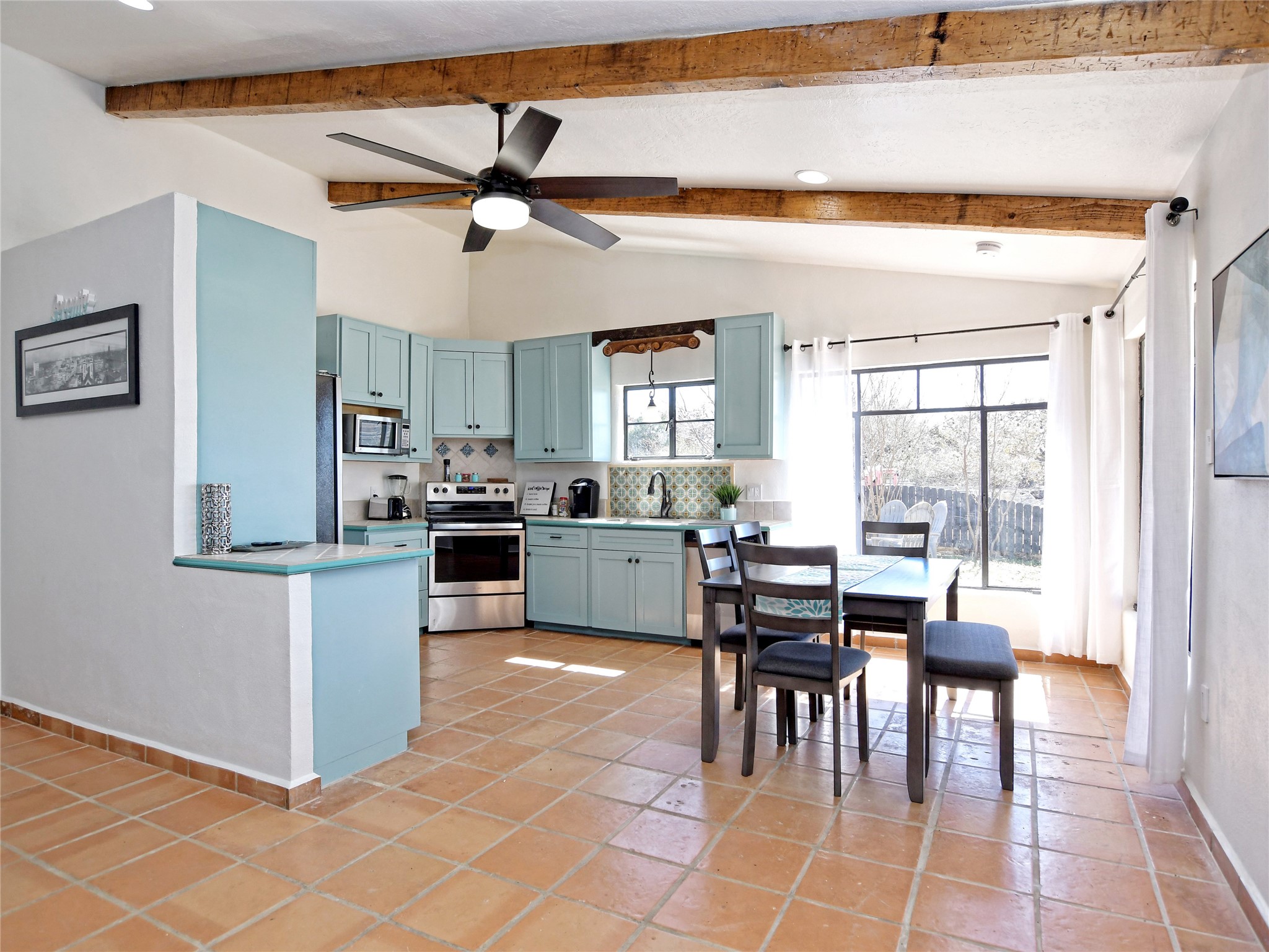 17123 Rocky Ridge Road Austin, TX 78734 - Photo 15 of 26 Kitchen and dining area featuring vaulted ceilings with exposed wood beams, light blue cabinetry with stainless steel appliances, terracotta tile flooring, and a large window overlooking outdoor scenery