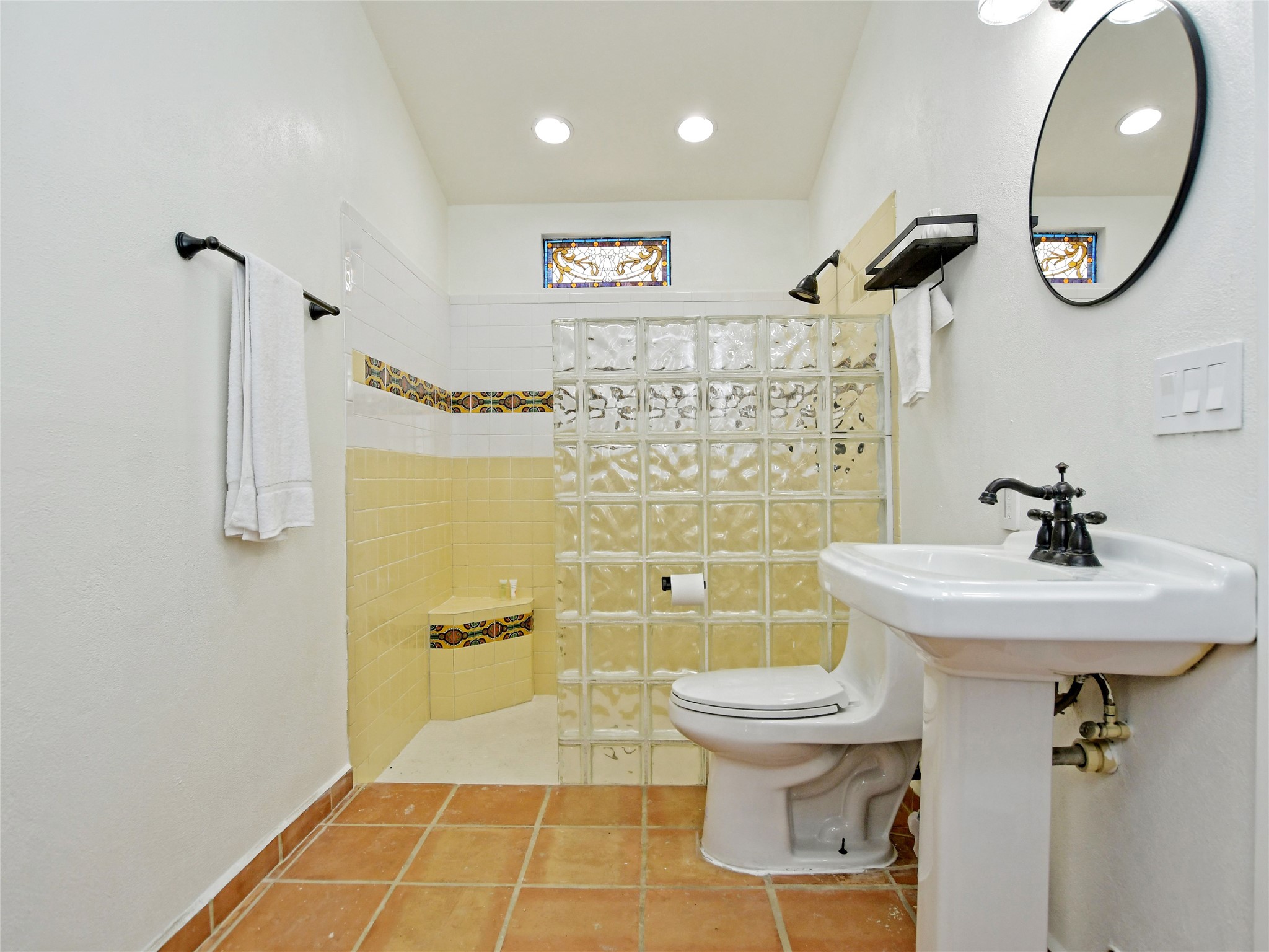 17123 Rocky Ridge Road Austin, TX 78734 - Photo 17 of 26 Bathroom featuring terracotta floor tiles, a pedestal sink with a dark bronze faucet, a glass block shower enclosure with a built-in bench, and a stained glass accent window