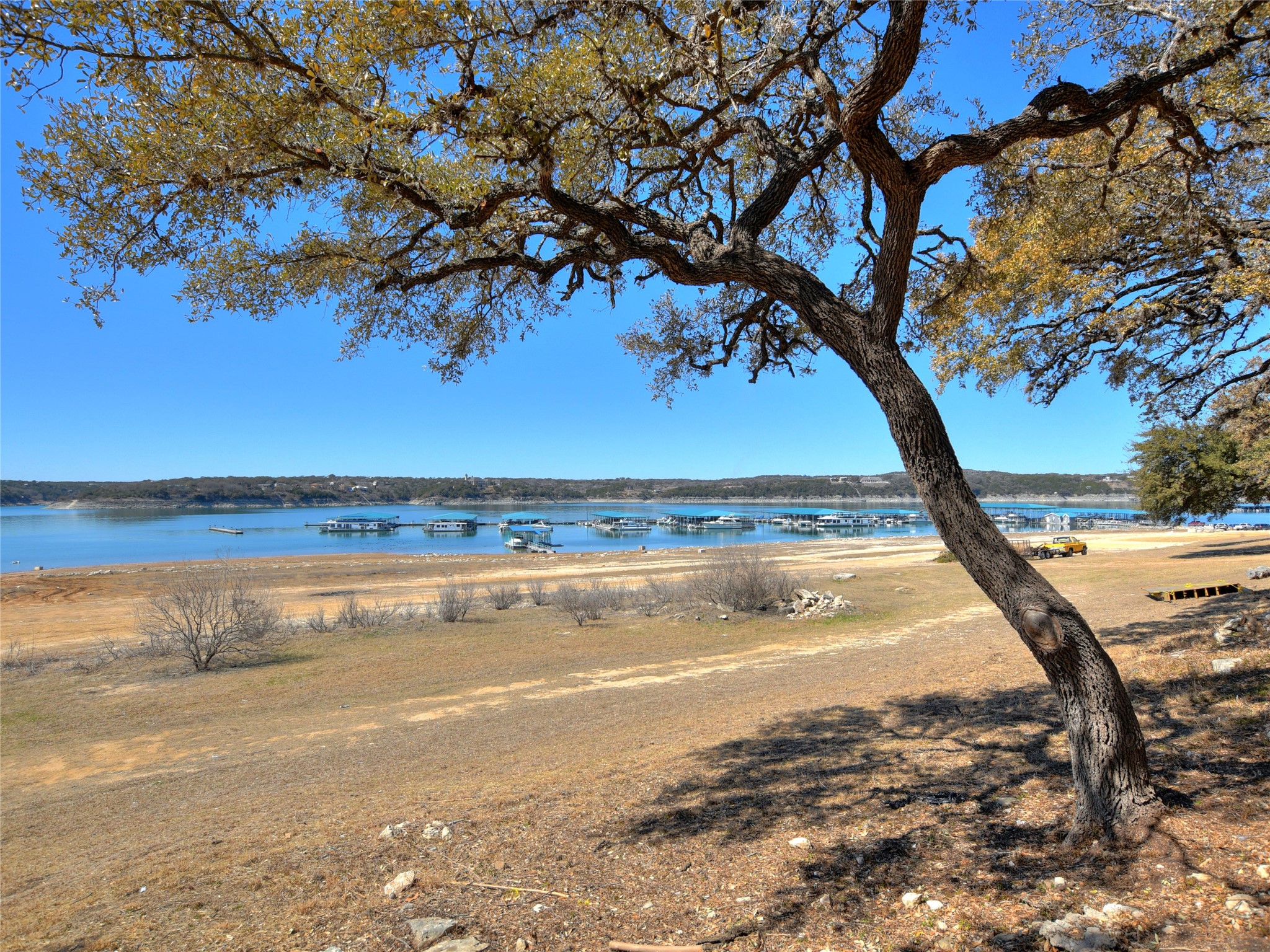 17123 Rocky Ridge Road Austin, TX 78734 - Photo 25 of 26 Waterfront property featuring a prominent tree with expansive branches, a wide shoreline, and a marina with multiple boats on the water