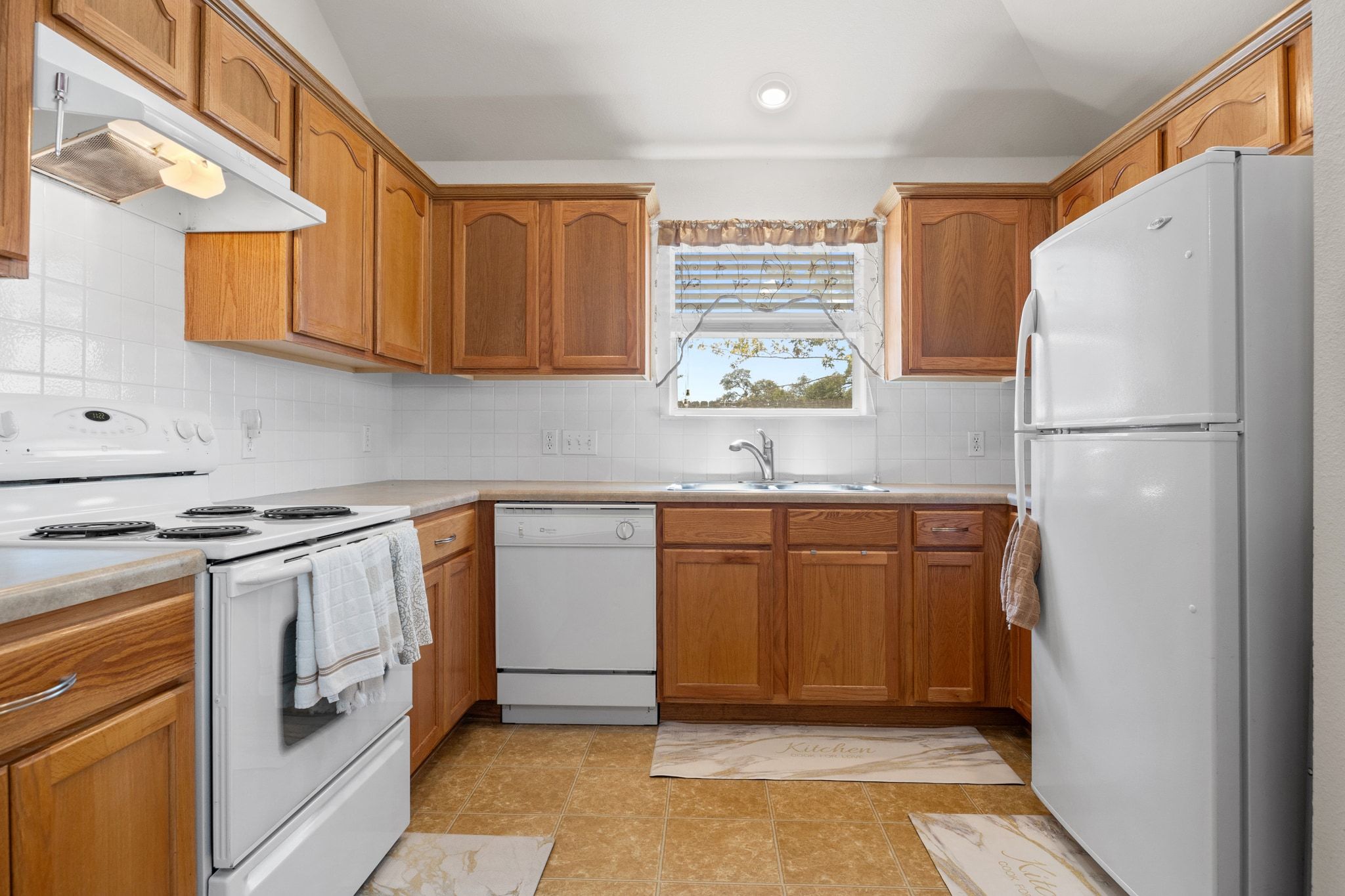 901 Kenneys Way Round Rock, TX 78665 - Photo 15 of 33 Kitchen with white appliances, decorative backsplash, under cabinet range hood, brown cabinets, and light countertops