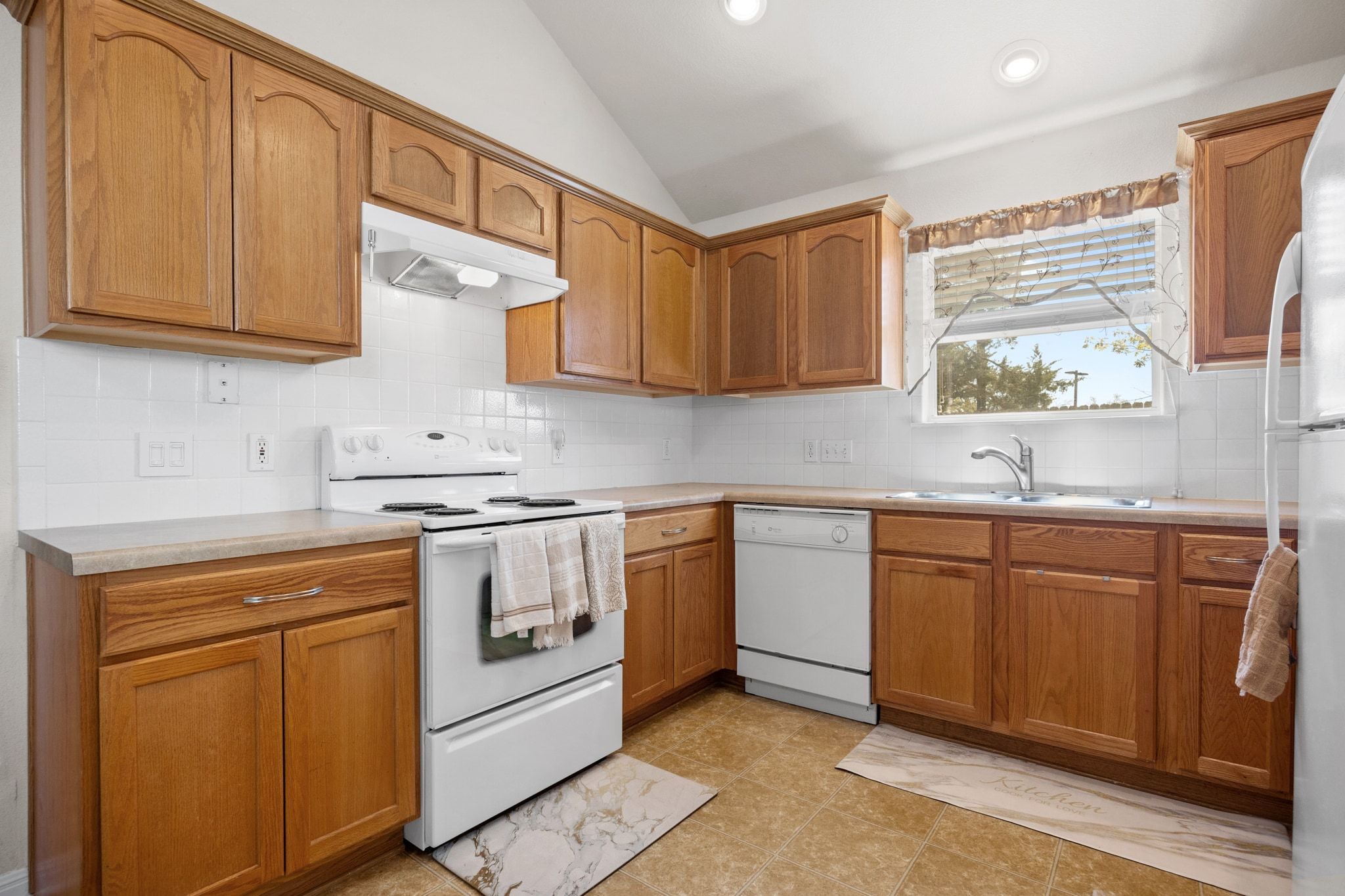901 Kenneys Way Round Rock, TX 78665 - Photo 18 of 33 Kitchen with white appliances, decorative backsplash, under cabinet range hood, brown cabinetry, and light countertops