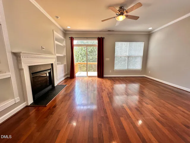a view of an empty room with wooden floor fireplace and a window