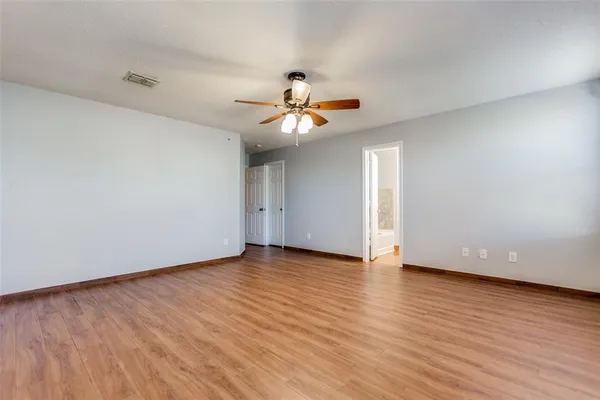 a view of an empty room with wooden floor and a ceiling fan