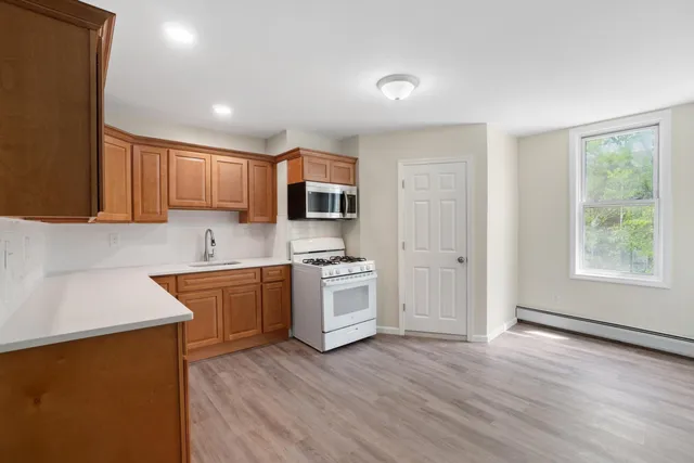 a kitchen with stainless steel appliances granite countertop a sink a stove a refrigerator cabinets and a wooden floor