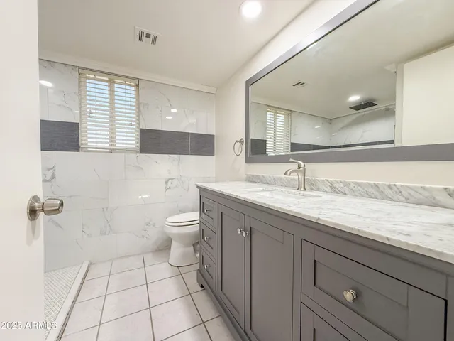 a spacious bathroom with a granite countertop sink a toilet a mirror and a shower