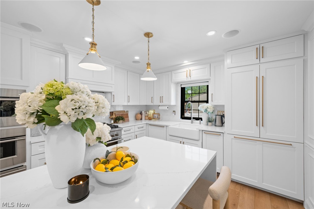 25870 Kennedy Ridge Road North Olmsted, OH 44070 - Photo 15 of 50 Bright kitchen featuring a central island with a light-toned countertop, white cabinetry with gold-toned hardware, wood-finish flooring, a farmhouse sink, and integrated panel-front appliances