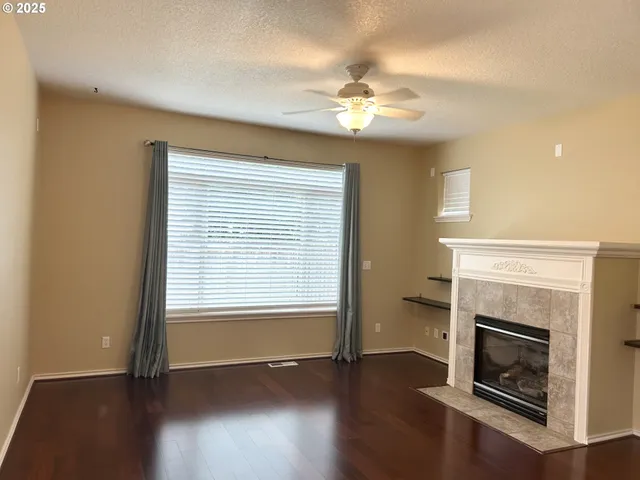 a view of an empty room with wooden floor fireplace and a window
