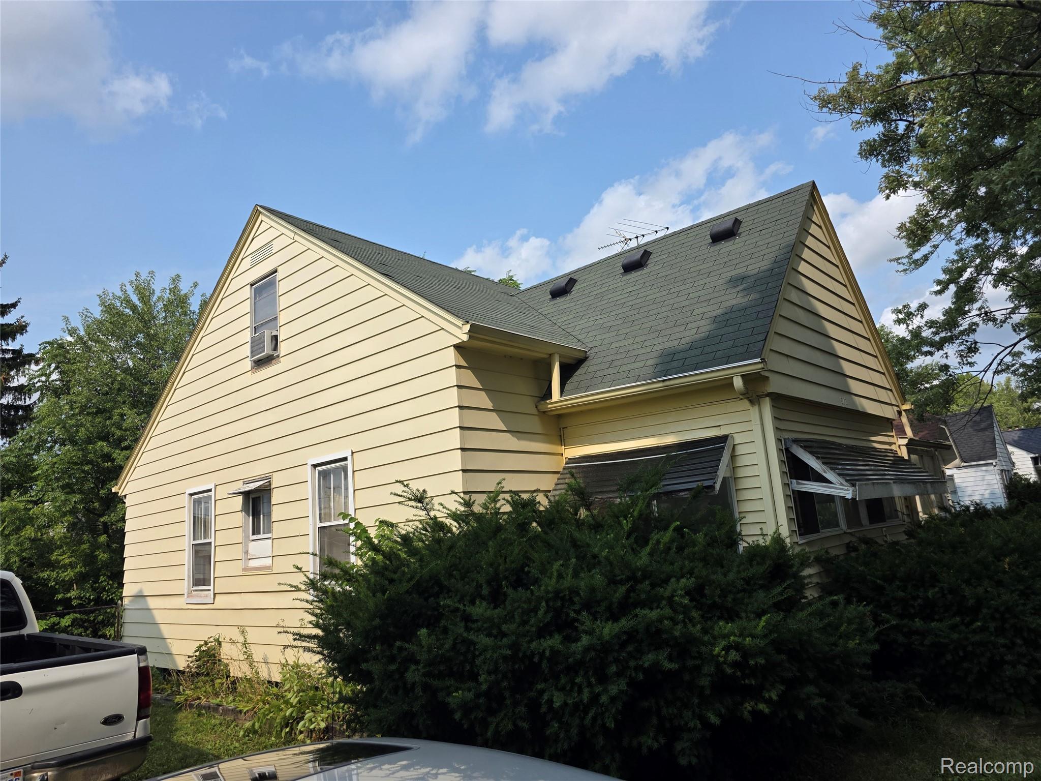 573 East Kennett Road Pontiac, MI 48340 - Photo 1 of 19 Classic Colonial-style home featuring cream-colored horizontal siding, a steeply pitched roof with dark asphalt shingles, and multi-pane windows