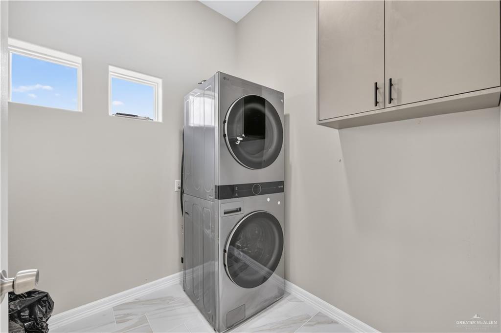 1920 Trinity Street Donna, TX 78537 - Photo 11 of 23 Dedicated laundry area featuring a stacked washer and dryer, upper cabinetry with black hardware, and two high windows