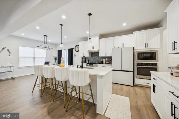 a kitchen with stainless steel appliances a refrigerator a stove a sink a dining table and chairs with wooden floor
