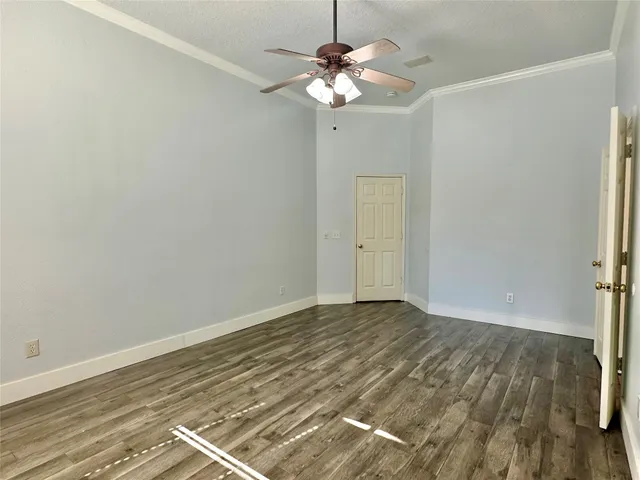 an empty room with wooden floor chandelier fan and windows