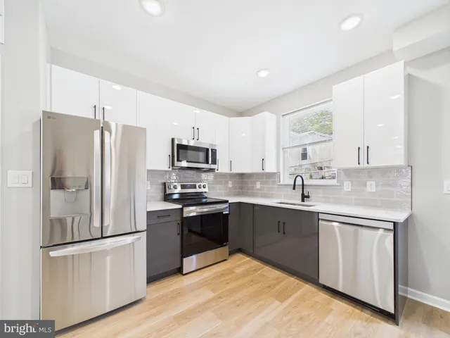 a kitchen with stainless steel appliances granite countertop a stove a sink dishwasher a refrigerator and white cabinets with wooden floor