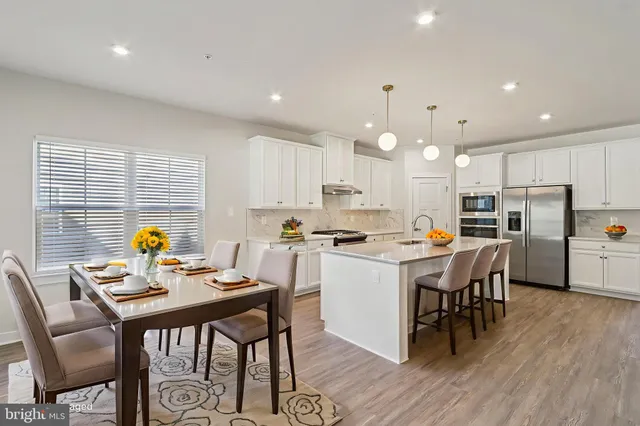 a kitchen with a dining table chairs appliances wooden floor and cabinets