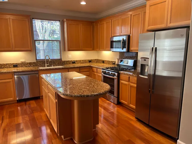 a kitchen with granite countertop stainless steel appliances a stove a sink a refrigerator cabinets and a window