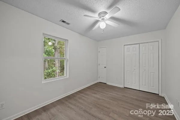 an empty room with wooden floor chandelier fan and windows