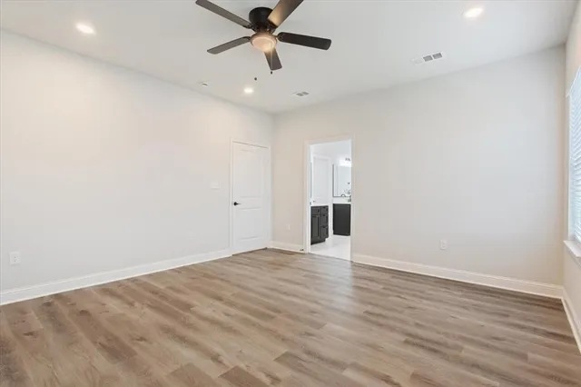 an empty room with wooden floor fan and windows