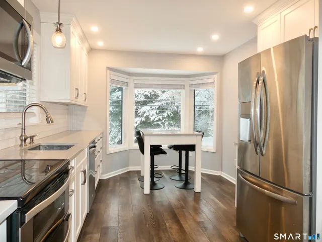 a kitchen with stainless steel appliances granite countertop a refrigerator a sink dishwasher a stove and a dining table with wooden floor