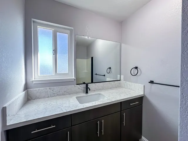 a bathroom with a granite countertop sink a mirror and shower