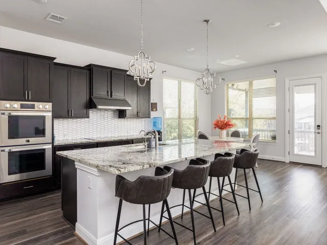 a kitchen with stainless steel appliances granite countertop a stove top oven a refrigerator a sink and white cabinets with wooden floor