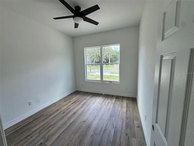 an empty room with wooden floor fan and windows
