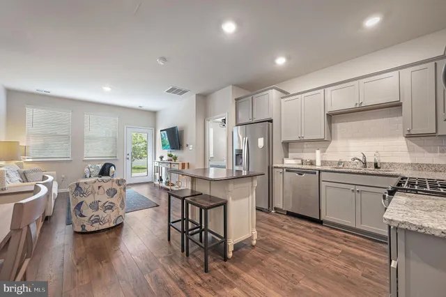 a kitchen with stainless steel appliances a stove a sink dishwasher a refrigerator with white cabinets and wooden floor