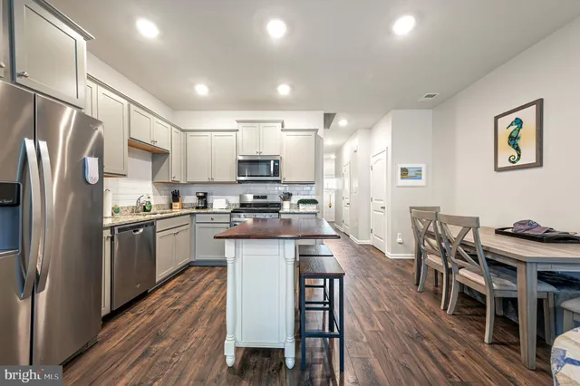 a kitchen with stainless steel appliances granite countertop a refrigerator a stove a sink a dining table and chairs with wooden floor