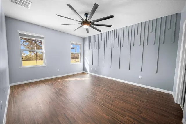an empty room with wooden floor chandelier fan and windows