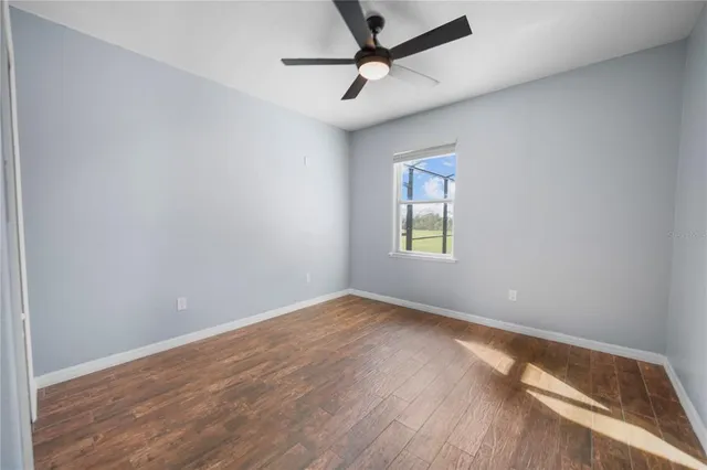 an empty room with wooden floor ceiling fan and windows
