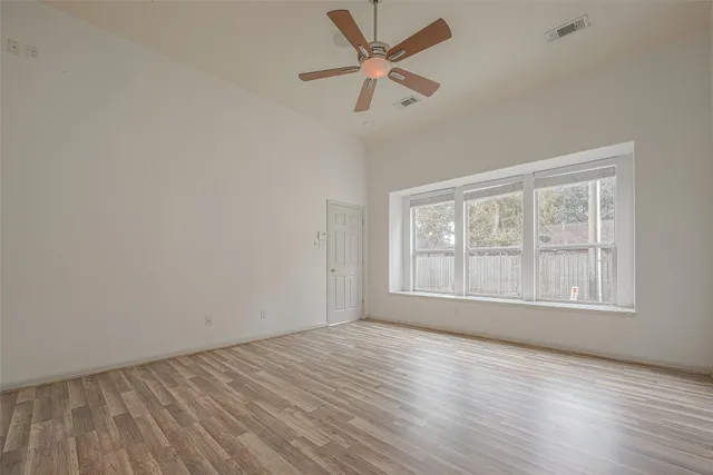 an empty room with wooden floor fan and windows