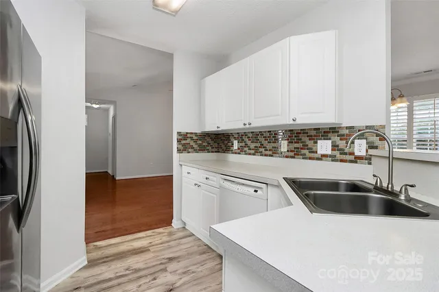 a kitchen with stainless steel appliances granite countertop a sink a refrigerator and white cabinets with wooden floor