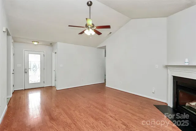 a view of an empty room with wooden floor fireplace and a window