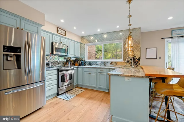 a kitchen with stainless steel appliances granite countertop a refrigerator a sink dishwasher a stove and white countertops with wooden floor