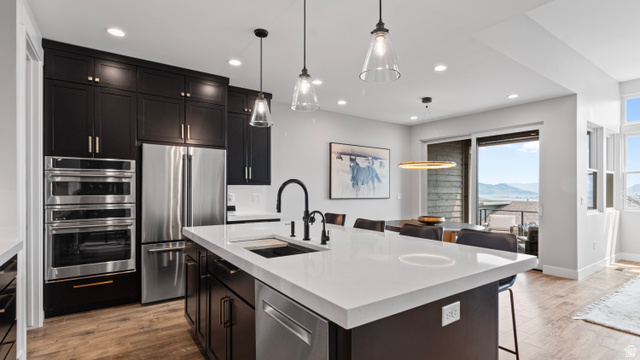 355 East Overlook Loop Hideout, UT 84036 - Photo 14 of 40 Modern kitchen featuring dark cabinetry, stainless steel appliances, a large center island with a white countertop, wood-finish flooring, and a sliding glass door opening to an outdoor space with mountain scenery