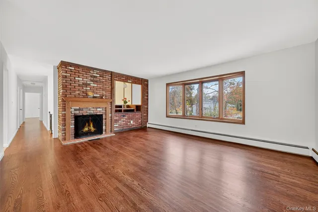 a view of an empty room with wooden floor fireplace and a window