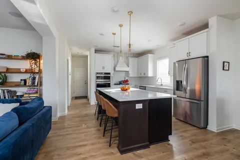 a kitchen with stainless steel appliances granite countertop a refrigerator a sink dishwasher a stove and a dining table with wooden floor