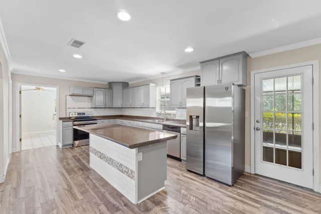 a kitchen with stainless steel appliances granite countertop a stove a refrigerator and a sink with wooden floors