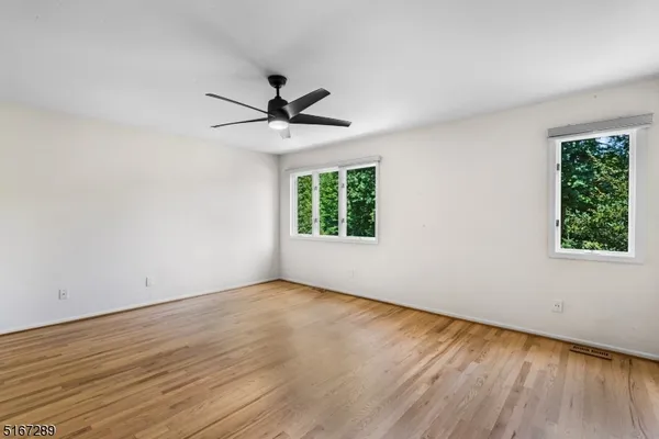 an empty room with wooden floor chandelier fan and windows