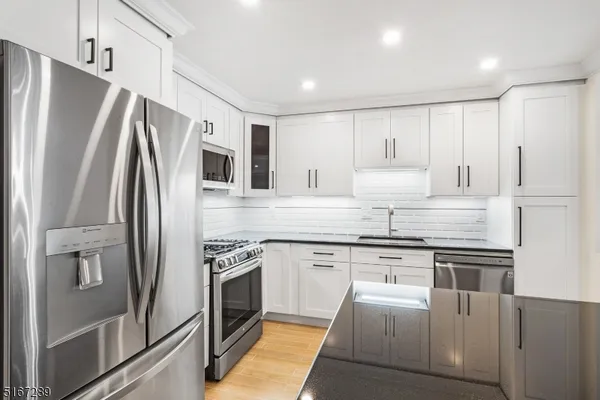a kitchen with stainless steel appliances granite countertop a refrigerator a stove a sink and white cabinets