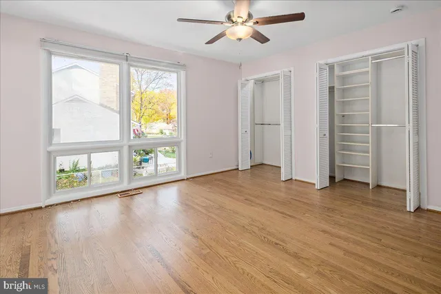 an empty room with wooden floor fan and windows