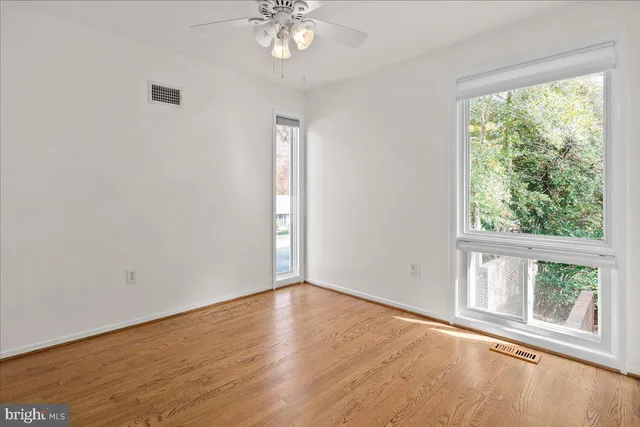 an empty room with wooden floor fan and windows