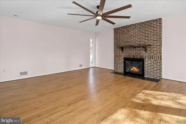an empty room with wooden floor fireplace and a ceiling fan