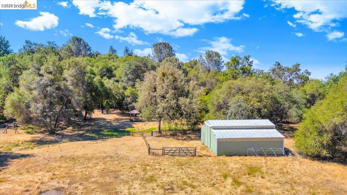 8733 Fraguero Road Sonora, CA 95370 - Photo 71 of 73 Expansive property featuring a green metal barn with a pitched roof, surrounded by mature trees and a natural landscape