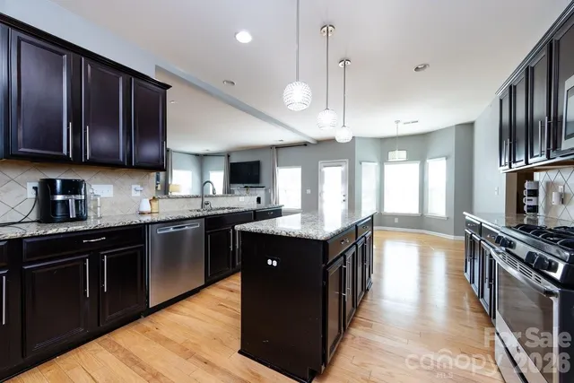 a kitchen with stainless steel appliances granite countertop wooden cabinets a sink dishwasher a stove and a refrigerator