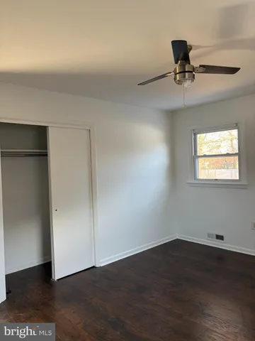 a view of an empty room with wooden floor and a ceiling fan