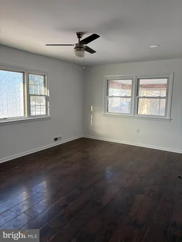an empty room with wooden floor fan and windows