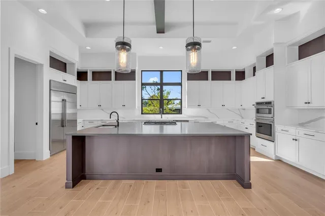 a large kitchen with stainless steel appliances a large counter top a sink a window and a refrigerator