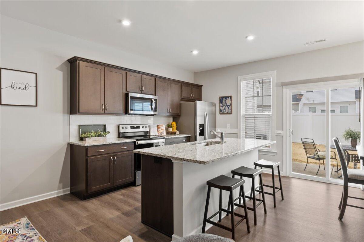 a kitchen with stainless steel appliances granite countertop a stove top oven a sink dishwasher a dining table and chairs with wooden floor